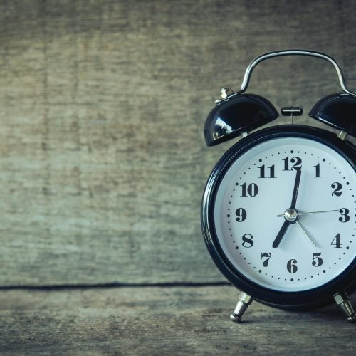 Classic black analog alarm clock on rustic wooden background, perfect for time and nostalgia themes.